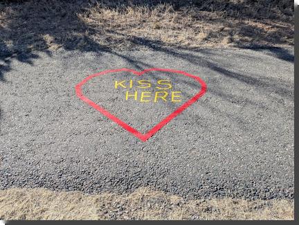 [On an asphalt path, KISS HERE in yellow tape surrounded by a red heart outline]