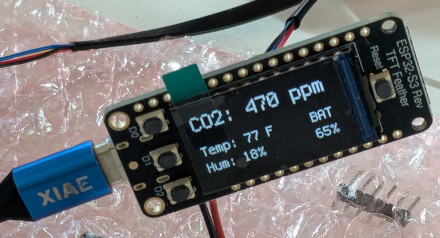[A small microcontroller with a built-in display reading CO2: 470ppm and some other stuff, plugged into a USB-C cable]