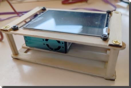 [a boxy blue air quality sensor in a crate made out of popsicle sticks, with a microcontroller with screen on top]