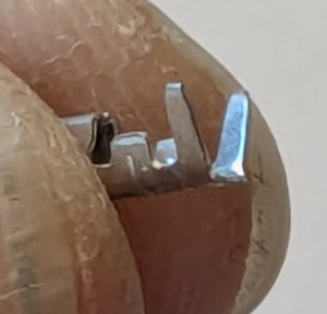 [the tips of a thumb and finger holding a small metal connector meant to be crimped]