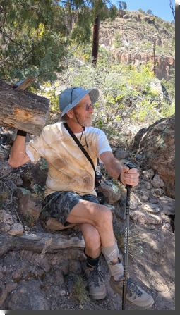 [A man sitting on a down ponderosa in a canyon, wearing a t-shirt that looks like tie-dye except the dye is all brown]