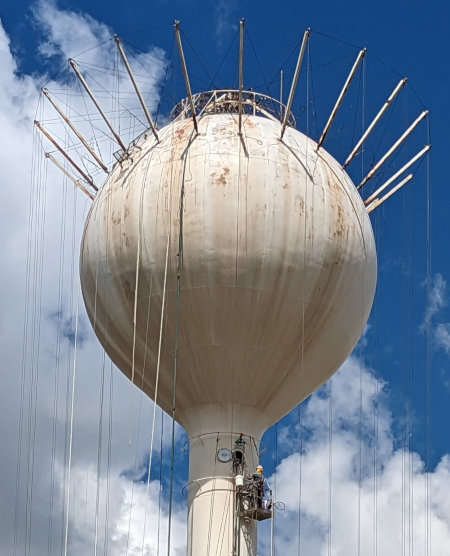 [Worker up high in basket under water tower]