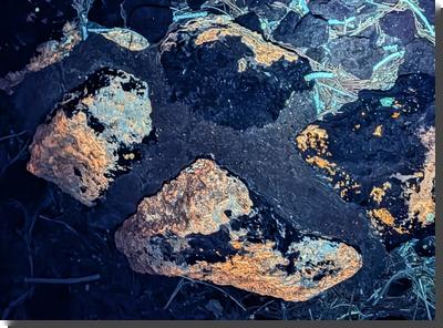 [assorted caliche-covered rocks fluorescing orange under UV light]
