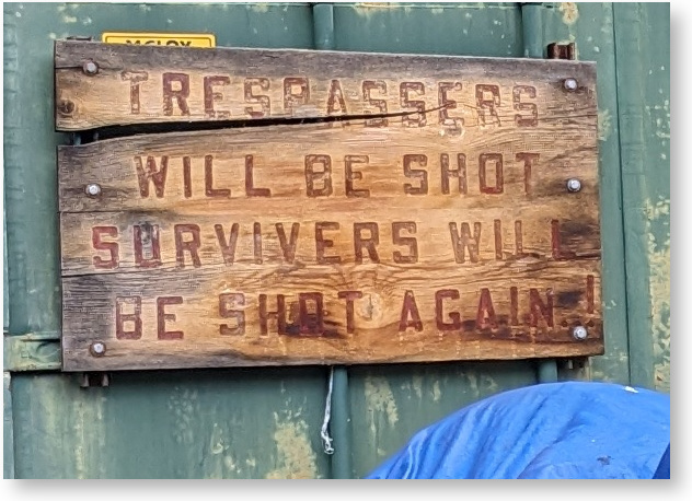 [Sign: Trespassers will be shot. Survivors will be shot again.]