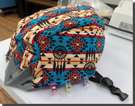 [an unfinished cloth cover over a bike helmet, made of cloth with a snazzy  blue and tan southwestern-inspired pattern, with sewing clips holding a part of the bottom turned under]