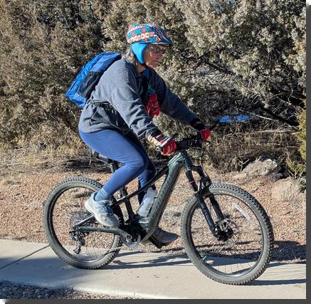 [the author on a bike, wearing a bike helmet covered with a blue and tan cloth cover, not completely finished, with fleece ear-warmers attached]